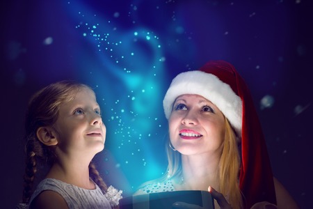 mother in Santa Claus cap and daughter opened a box with Christmas gift boxes of shining light and...
