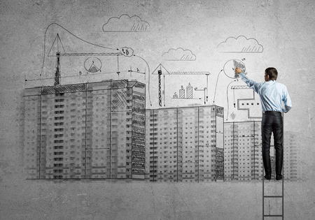 Rear view of businessman standing on ladder and drawing buildingsの写真素材