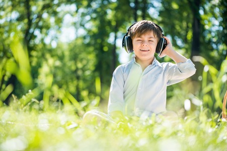 Young joyful boy in summer park wearing headphonesの写真素材