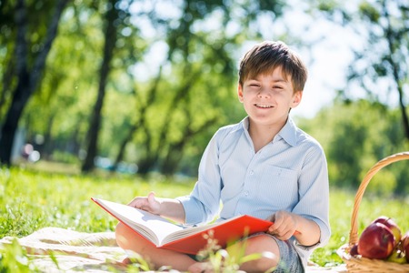 Little adorable boy in sitting park with book in handsの写真素材