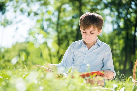 Little adorable boy in sitting park with book in handsの写真素材