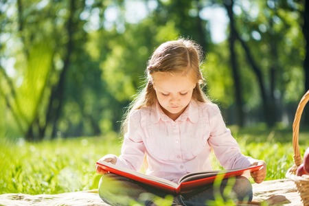 Adorable girl in summer park reading bookの写真素材