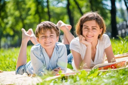 Cute boy and young woman in summer park laying on grassの写真素材