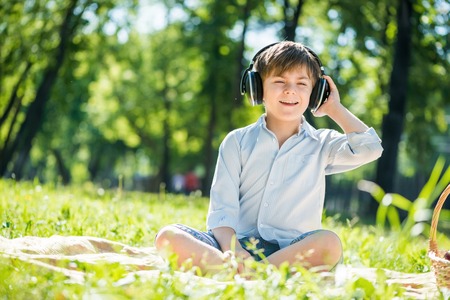 Young joyful boy in summer park wearing headphonesの写真素材