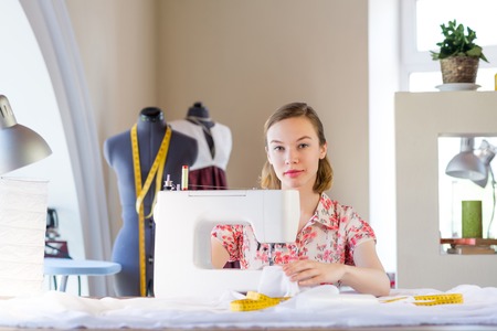 Young attractive needlewoman at studio working with sewing machine