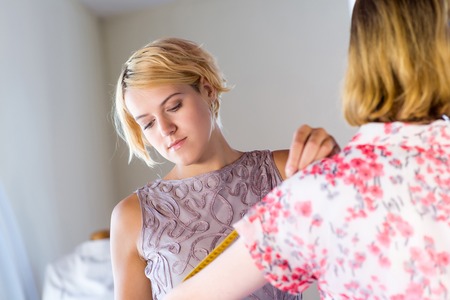 Young needlewoman taking measures of female clientの写真素材