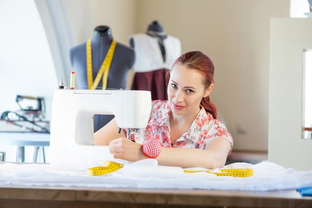 Young attractive needlewoman at studio working with sewing machine