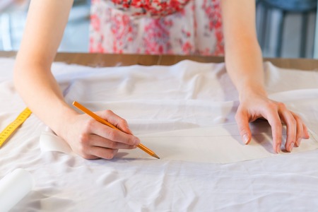 Close up of tailors hands drawing with pencil on fabricsの写真素材