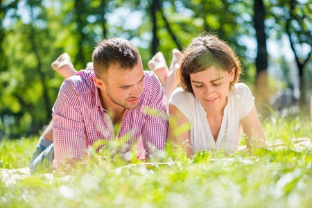 Young romantic couple lying in park and reading bookの写真素材