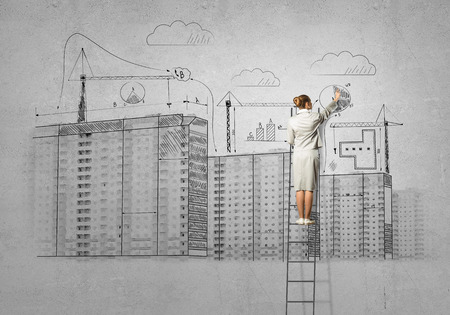 Rear view of businesswoman standing on ladder and drawing on wallの写真素材