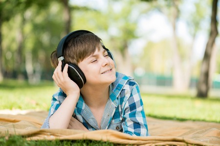 Cute boy of school age in park wearing headphonesの写真素材