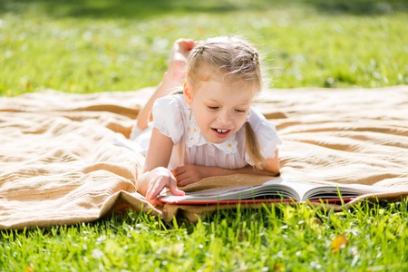 Little cute girl in summer park reading bookの写真素材