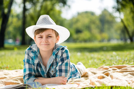 Cute boy in summer park lying on blanket and reading bookの写真素材