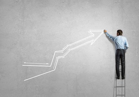 Rear view of businessman standing on ladder and drawing graphの写真素材