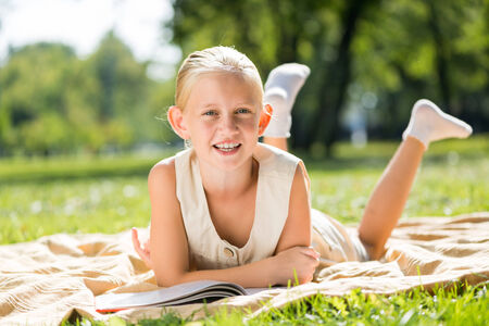 Little cute girl in summer park reading bookの写真素材
