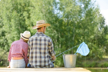 Back view of father and daughter sitting on pier and fishingの写真素材