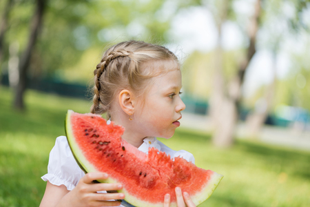 Cute girl sitting in park and eating watermelonの写真素材