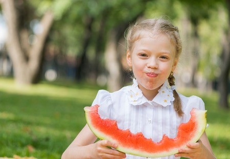Cute girl sitting in park and eating watermelonの写真素材