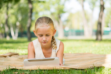 Cute girl lying in park and using tablet pcの写真素材