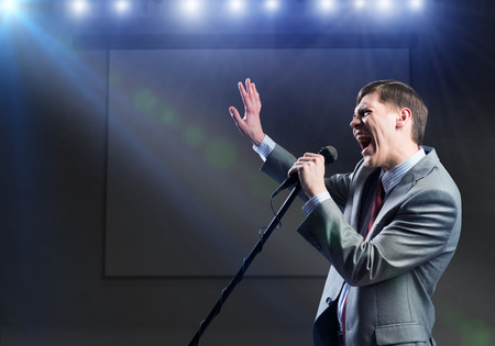 Young handsome businessman sining on stage in microphoneの写真素材