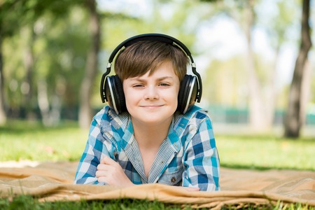 Cute boy of school age in park wearing headphonesの写真素材