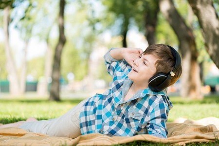 Cute boy of school age in park wearing headphonesの写真素材