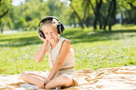 Cute girl wearing headphones sitting in summer parkの写真素材