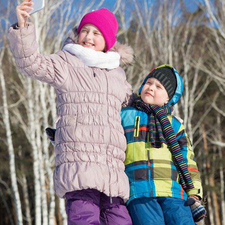 Two happy kids making selfie photo in winter parkの写真素材
