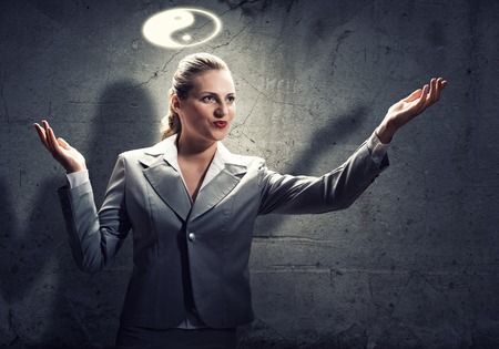 Young gesturing businesswoman with yin yang sign above headの写真素材