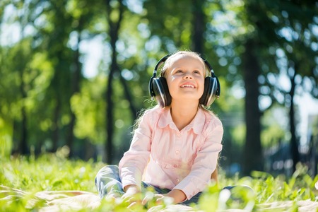 Little cute girl in summer park listening musicの写真素材