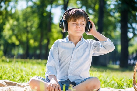 Young joyful boy in summer park wearing headphonesの写真素材