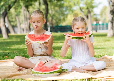 Two cute girls sitting in park and eating watermelonの写真素材