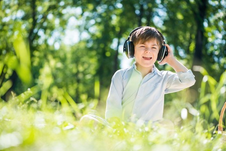 Young joyful boy in summer park wearing headphonesの写真素材