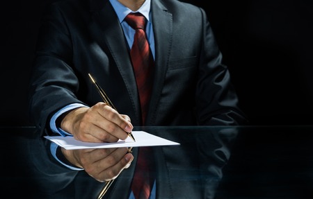 Close up of businessman sitting at table and signing documentの写真素材
