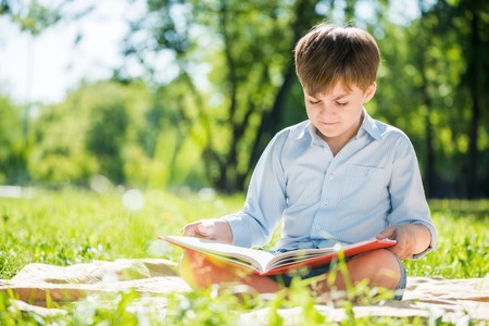 Little adorable boy in sitting park with book in handsの写真素材