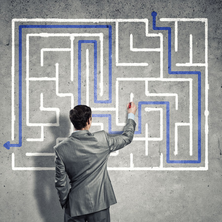 Back view of businessman drawing labyrinth on wallの写真素材
