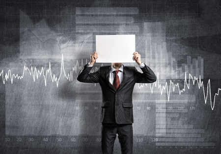 Businessman and graphs at background hiding his face behind paperの写真素材