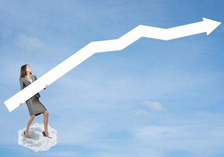Young businesswoman standing on cloud holding white arrowの写真素材