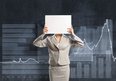 Businesswoman and graphs at background hiding her face behind paperの写真素材