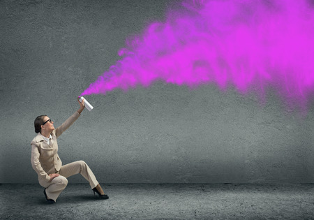 Young businesswoman with suitcase using spray balloonの写真素材