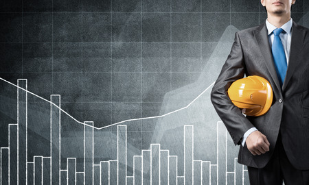 Close up of businessman with helmet in hand and graphs at backgroundの写真素材