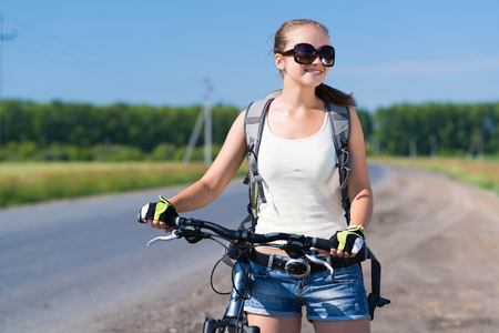Young pretty woman with backpack riding bicycle outdoorsの写真素材