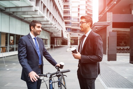 Businessmen talking while walking with bicycle outdoorsの写真素材