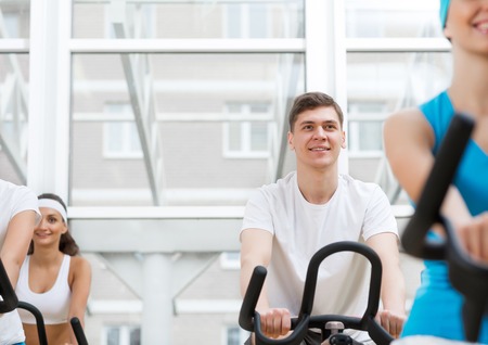 Small group of young people exercising on bikes in fitness centerの写真素材