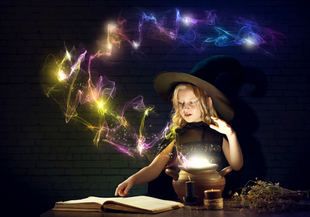 Little Halloween witch reading conjure from magic book above potの写真素材