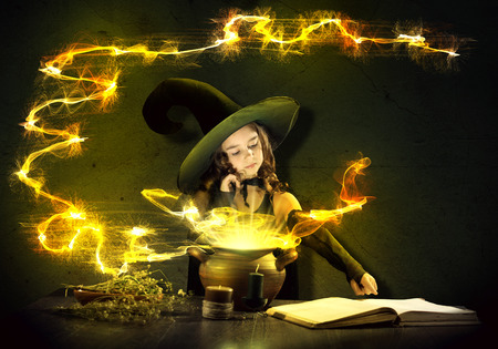 Little Halloween witch reading conjure from magic book above potの写真素材