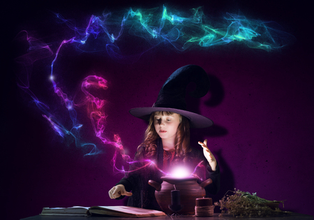Little Halloween witch reading conjure from magic book above potの写真素材