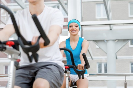 Small group of young people exercising on bikes in fitness centerの写真素材