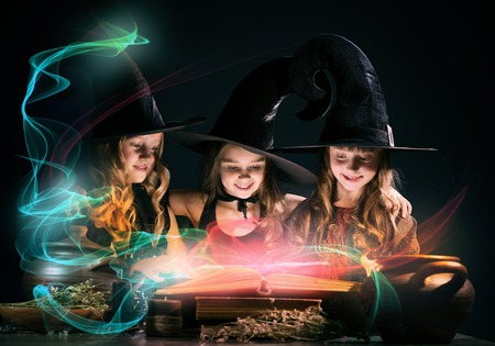 Three little Halloween witches reading conjure from magic bookの写真素材