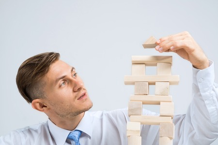 Young handsome businessman building tower of wooden blocksの写真素材
